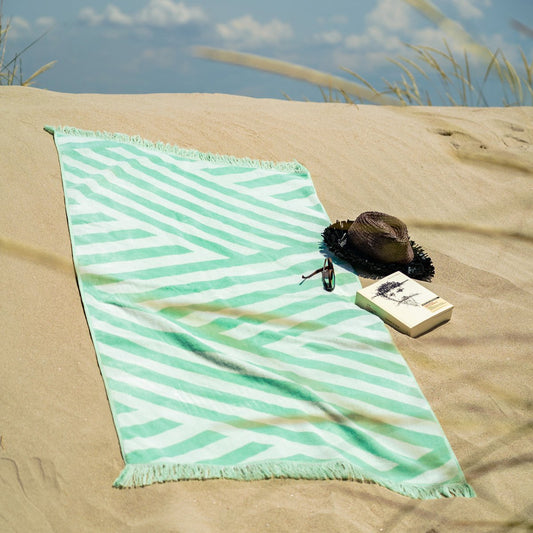 Strandhanddoek Groen met subtiele streepjesmotief op zandstrand, ideaal voor stranddagen of zwembadgebruik in de zomer.